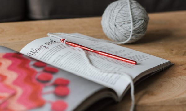 Crochet hook, yarn, and a pattern book, photographed by Anete Lusina